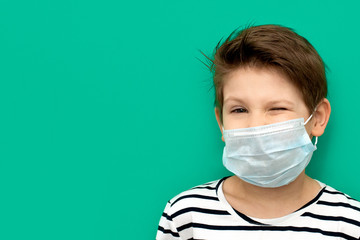 Boy winks in medical mask isolated during coronovirus. Emotions of surprise. Copy space. Green color