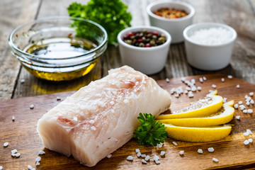 Fresh raw cod with seasonings and vegetables served on cutting board on wooden table