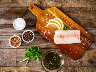 Fresh raw cod with seasonings and vegetables served on cutting board on wooden table