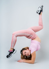 Smiling acrobat woman wearing pink sportswear working out in the studio isolated on gray background