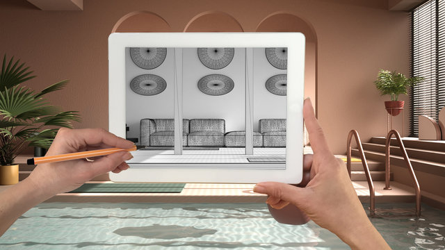 Hands holding and drawing on tablet showing colored contemporary living room with swimming pool CAD sketch. Real finished interior in the background, architecture design presentation