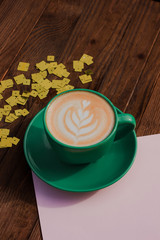 Layout with coffee. Cappuccino. Shiny sequins and pink paper on a wooden background. Flower drawn on coffee. Flat lay 