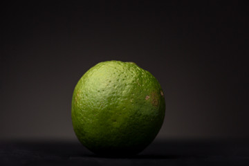Closeup showing the texture and detail of a fresh vibrant green lime fruit contrasted against a dark grey background