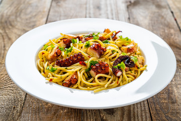 Spaghetti with fried octopus on wooden table