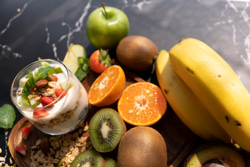 Healthy foods Consist of yogurt in a glass of cereal green apples, strawberry, almonds and mint leaves to sprinkle on the black marble background. Conceptual of healthy food for good life.