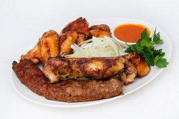 Grilled chicken wings, cradles of women, grilled meat, chopped onion rings, parsley, and meat sauce on an oval white plate on a white plate