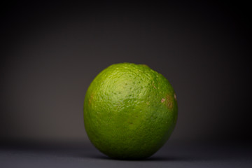 Isolated vibrant fresh green lime fruit contrasted against a dark grey background