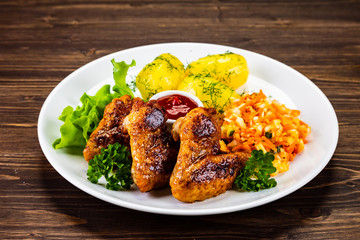 Fried chicken wings with boiled potatoes and vegetable salad on wooden board