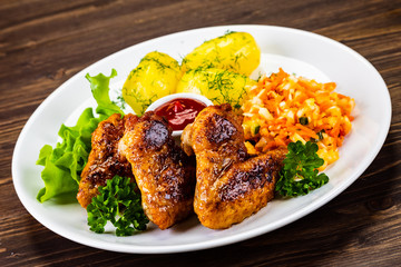 Fried chicken wings with boiled potatoes and vegetable salad on wooden board