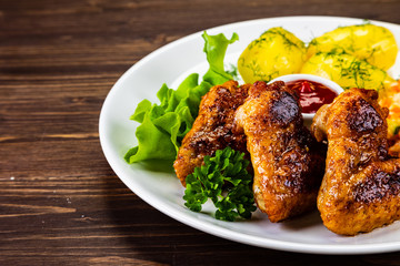 Fried chicken wings with boiled potatoes and vegetable salad on wooden board