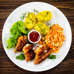Fried chicken wings with boiled potatoes and vegetable salad on wooden board