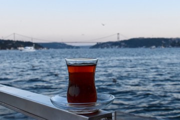 Having a Turkish tea in a traditional glass by the sea with the view of Bosporus Bridge