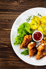 Fried chicken wings with boiled potatoes and vegetable salad on wooden board
