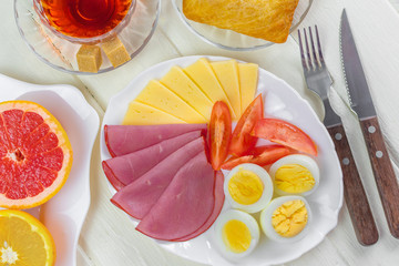 Fresh delicious breakfast with soft boiled egg, cheese, ham fresh bread and cup coffee or tea on light wooden background.