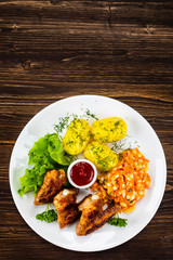 Fried chicken wings with boiled potatoes and vegetable salad on wooden board