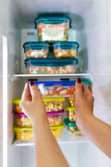 Woman placing container with frozen mixed vegetables in freezer.