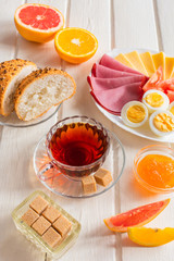 Fresh delicious breakfast with soft boiled egg, cheese, ham fresh bread and cup coffee or tea on light wooden background.