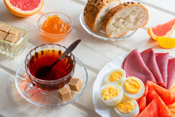 Fresh delicious breakfast with soft boiled egg, cheese, ham fresh bread and cup coffee or tea on light wooden background.