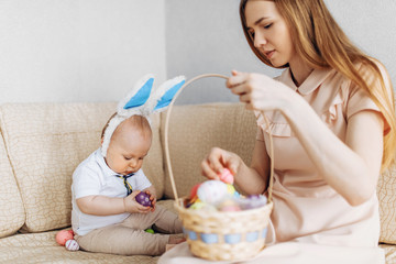 Mother and baby with rabbit ears, with Easter eggs in a basket, parents and children play indoors. Family celebrates Easter,