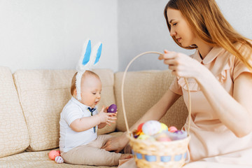 Mother and baby with rabbit ears, with Easter eggs in a basket, parents and children play indoors. Family celebrates Easter,