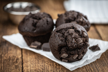 Old wooden table with fresh Chocolate Muffins (close-up shot; selective focus)