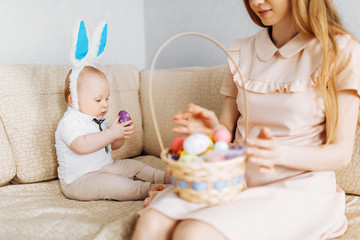 Mother and baby with rabbit ears, with Easter eggs in a basket, parents and children play indoors. Family celebrates Easter,