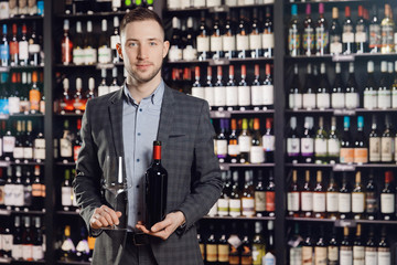 Sommelier man holds bottle red wine and glass on dark background restaurant