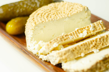 Smoked cottage cheese, brined cheese cut with pickled cucumber on a wooden plate