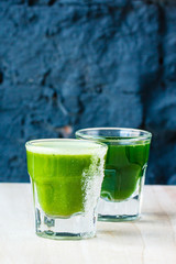 Green smoothie made from herbs and vegetables in a large glass glass against a dark stone wall