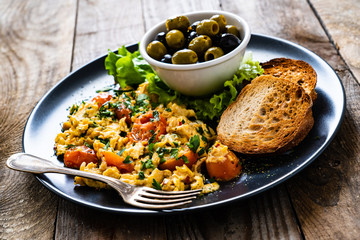 Breakfast - scrambled eggs with vegetables and toasted bread on wooden background