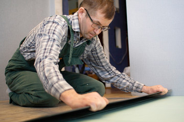 A worker puts a new laminate on the floor. Laying the floor covering. Master in the house.
