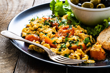 Breakfast - scrambled eggs with vegetables and toasted bread on wooden background