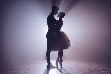 Romantic professional ballet pair looking to each other on dark stage. Young couple dancing in...