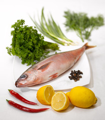raw fish lemon, pepper and greens on the kitchen table