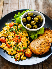 Breakfast - scrambled eggs with vegetables and toasted bread on wooden background