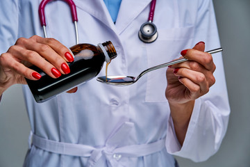 Female doctor with a phonendoscope on her neck pours medicine into a spoon. Medical concept