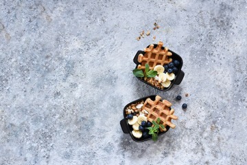 Belgian waffles with yogurt, granola, banana and blueberry for breakfast on a concrete background. View from above.