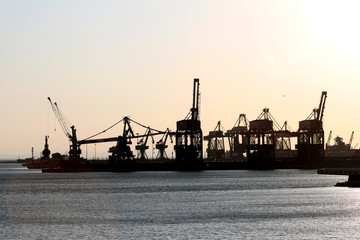 Fototapeta na wymiar Taranto merchant port at sunset. Silhouette of harbor cranes. Puglia, Italy