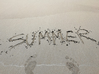 The inscription Summer on the sand of the beach and footprints. the concept of leisure holiday