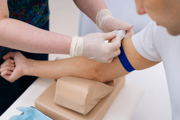 Obraz na płótnie Canvas Nurse tightening the medical tourniquet on arm before taking blood sample. Preparation for blood test with by phlebotomist technician doctor. Concept of healthcare and medicine.