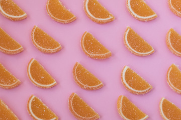 Marmalade slices of orange and lemon laid in oblique rows on a pink background