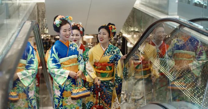 Three beautful japanese geishas in traditional kimono dresses walking in shopping cenre, standing in escalator and chatting - traditional culture in modern japan 4k footage