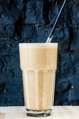 Brown Smoothie or cocktail with coffee and yogurt in a large glass glass against a dark stone wall