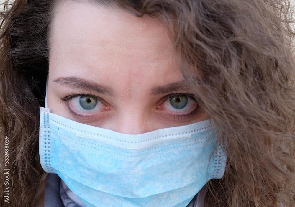 Wall mural the girl's face with curly hair in a medical mask closeup. the emotions of the patient