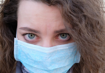 The girl's face with curly hair in a medical mask closeup. the emotions of the patient