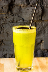 Green smoothie made from herbs and vegetables in a large glass glass against a dark stone wall