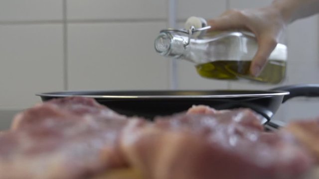 Selective focus shot, as pouring oil into a frying pan, delicious meat in the blurred foreground.