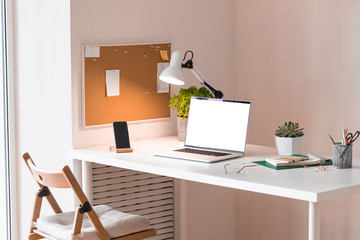 Laptop with blank white screen on office desk interior. Stylish rose gold workplace mockup table...
