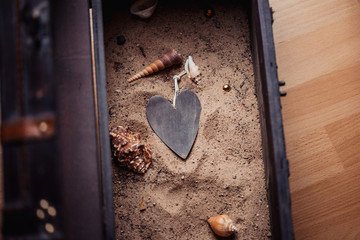 Liebe, Schatz, Schatztruhe - Herz aus Holz in Sand mit Muscheln in Schatztruhe