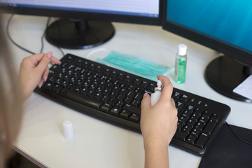 Female hands spray disinfectant spray on computer keyboard. Antibacterial processing of office equipment